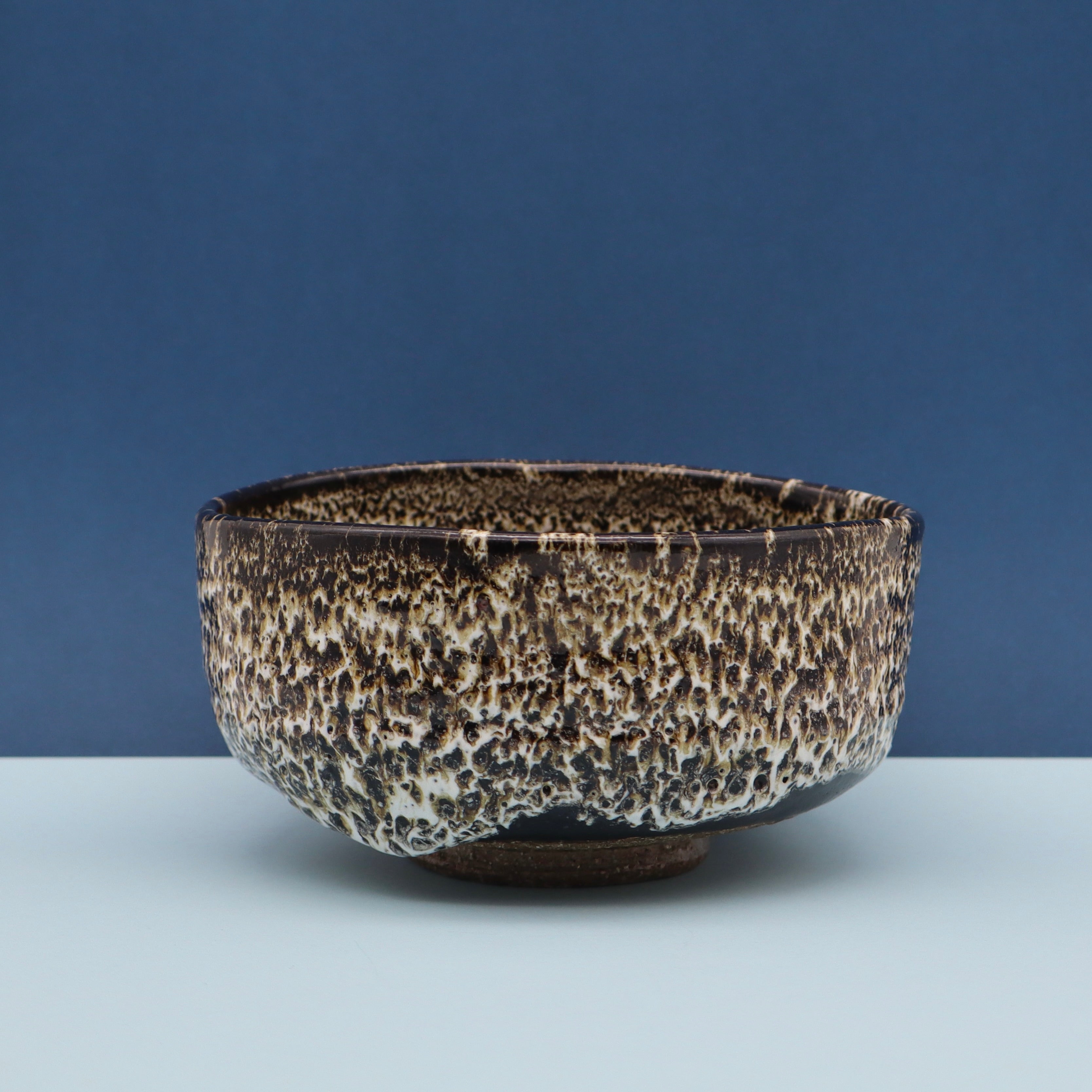 Handcrafted Japanese matcha kutsugata chawan tea bowl from Aichi, Japan, beautiful white and black drip glaze, blue background, front view