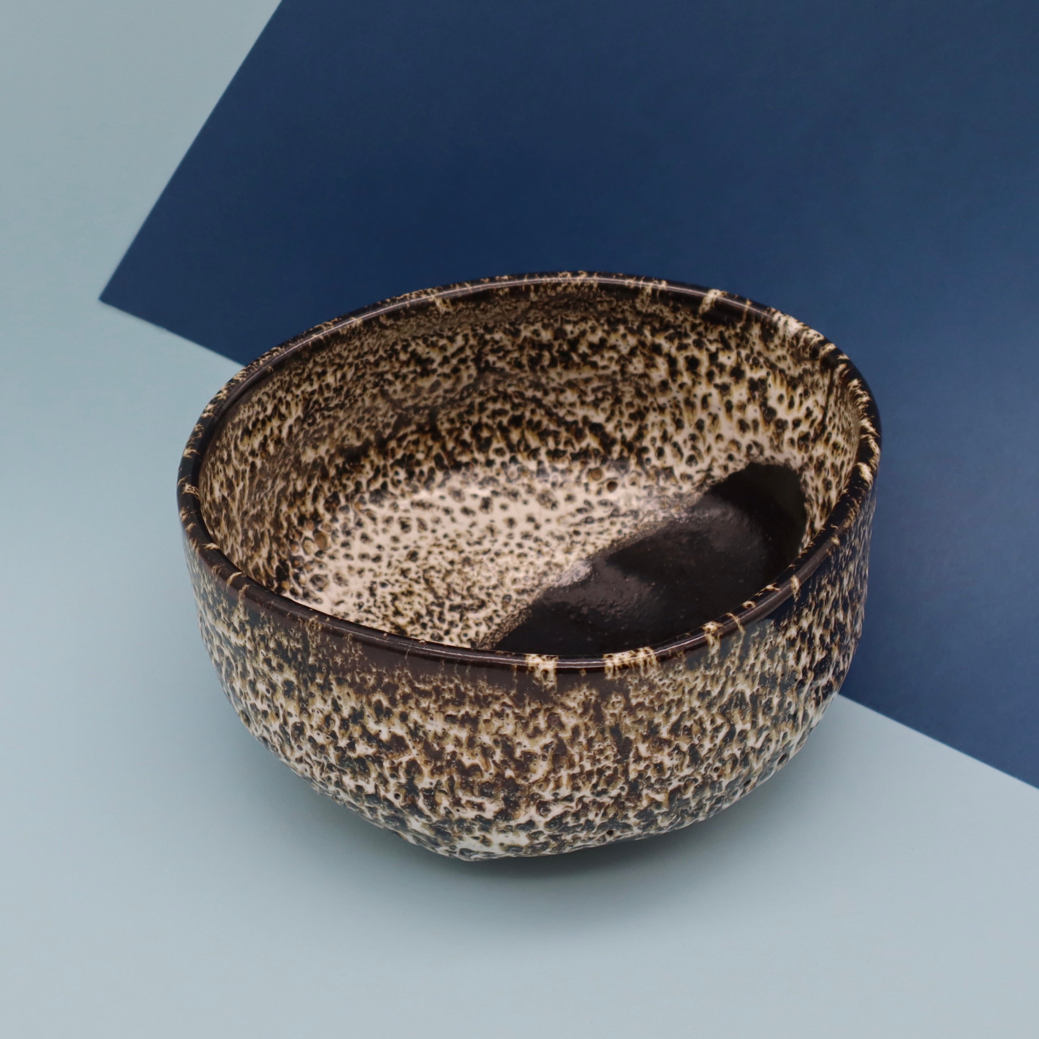 Handcrafted Japanese matcha kutsugata chawan tea bowl from Aichi, Japan, top view organic handmade shape, blue background, angled view