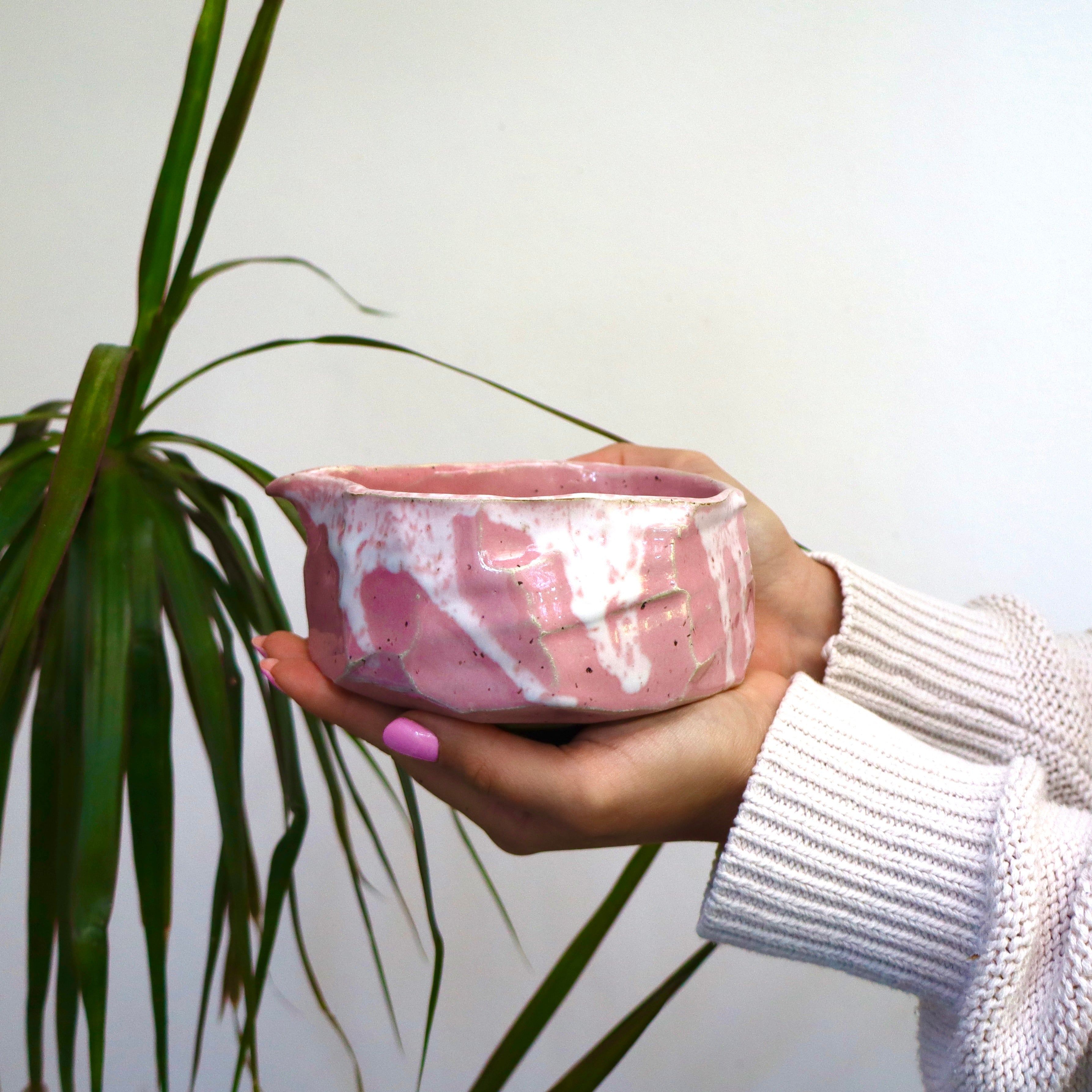 Woman's hands with pink nails holding a Pink kurinuki matcha chawan with spout - wabi sabi tea bowl front view