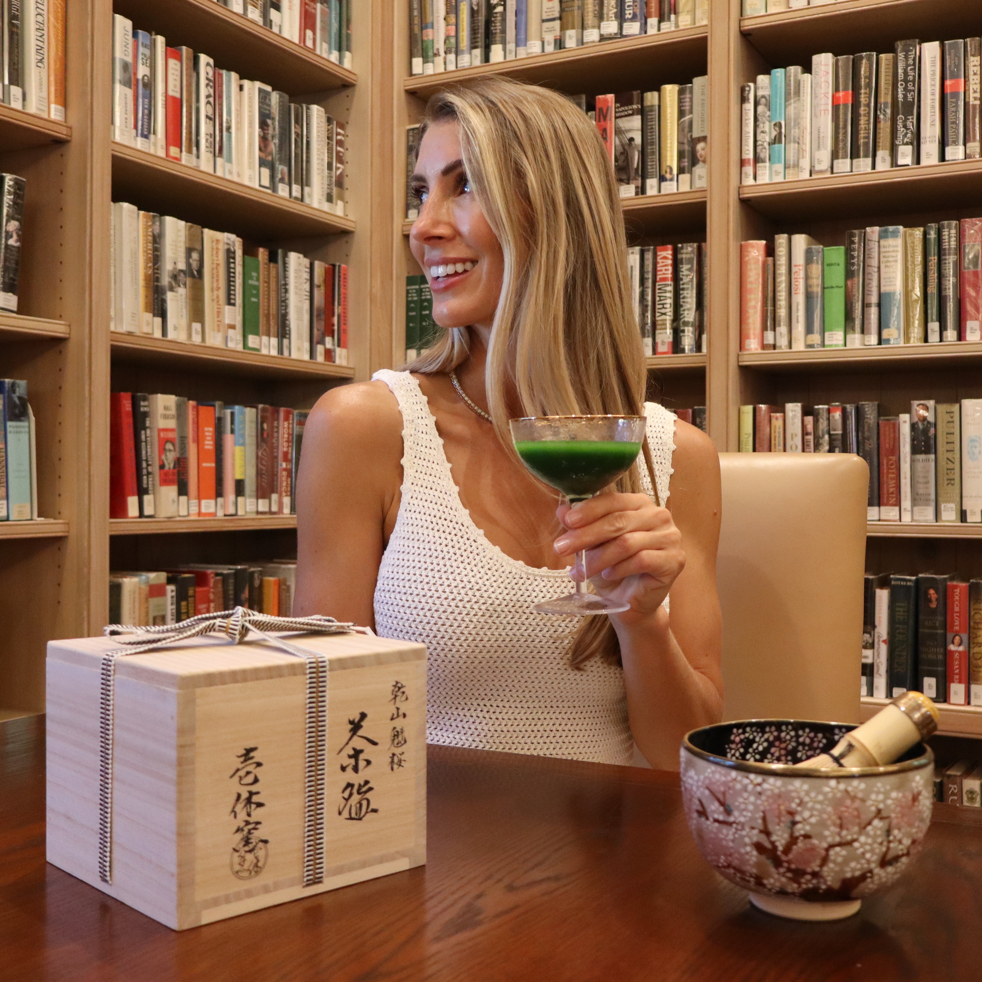 Woman sitting at a table in a library with a drink and a box of tea.